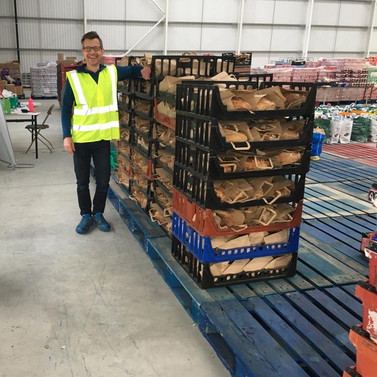 A photo of one of the worker at the Leeds City Council emergency food packages drop off stood next to several crates of Leeds Bread Co-op loaves