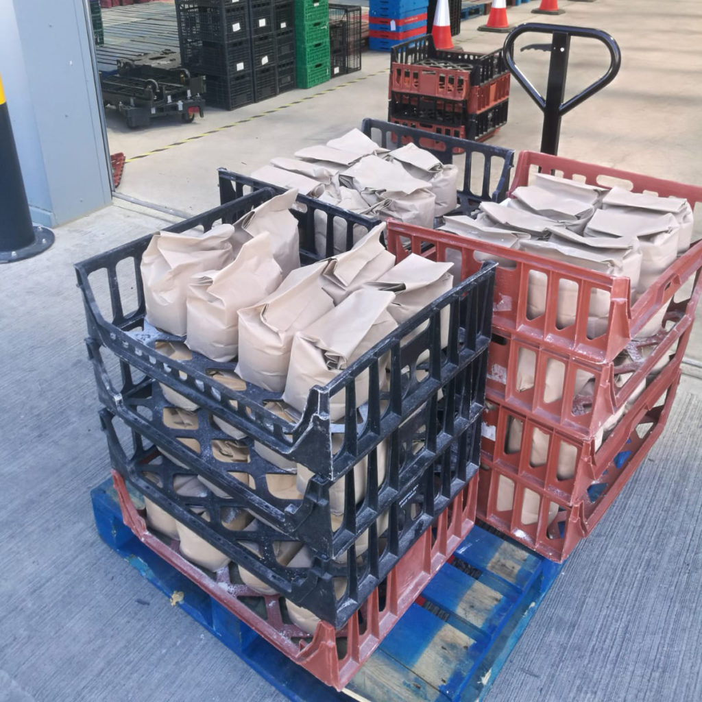 A palette of crates with many brown bags filled with flour being donated to emergency food packages