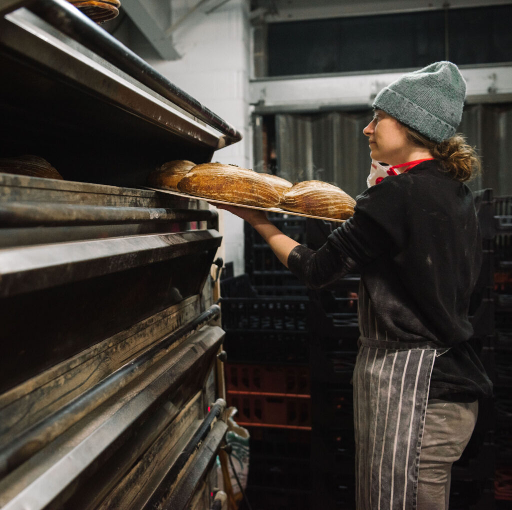 A photo of baker Karen taking some perfectly baked loaves of white sourdough out of the oven. 