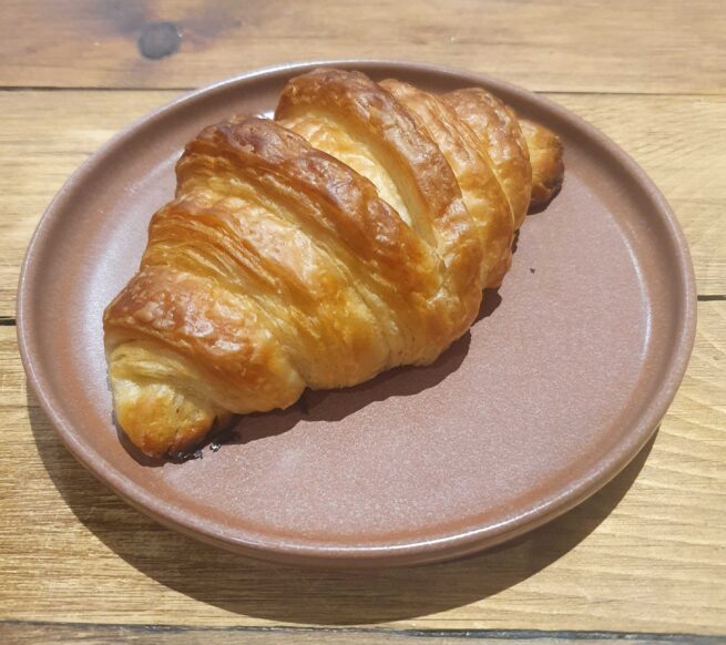 A vegan croissant with a 'v' shape in the pastry on top, on a pastel pink plate.