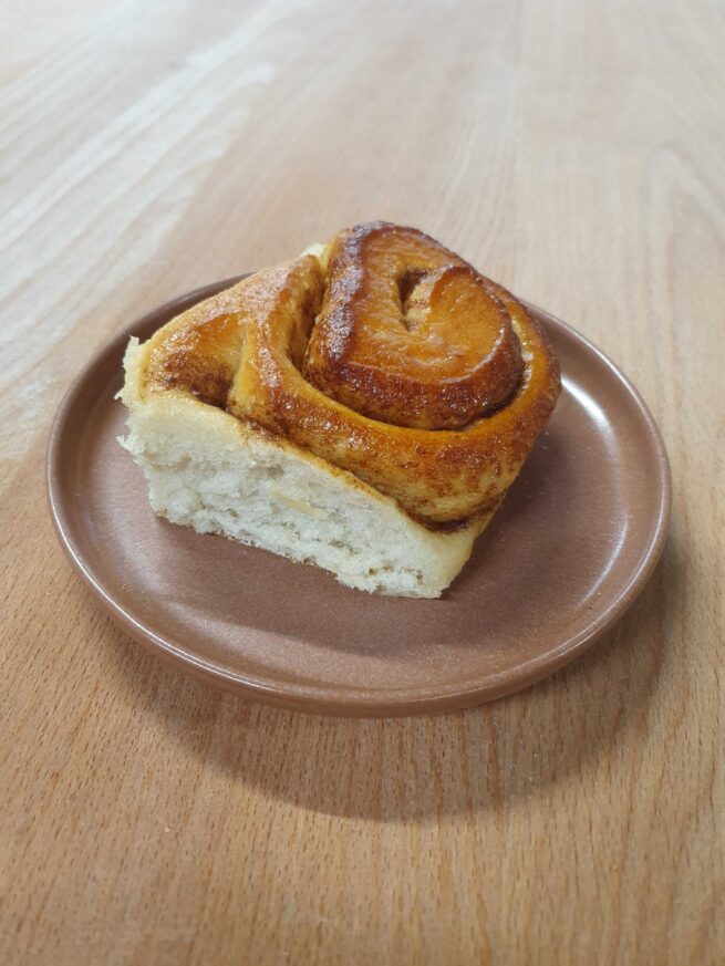 Cinnamon Bun - a golden brown swirl, tall and fluffy on a pink plate.